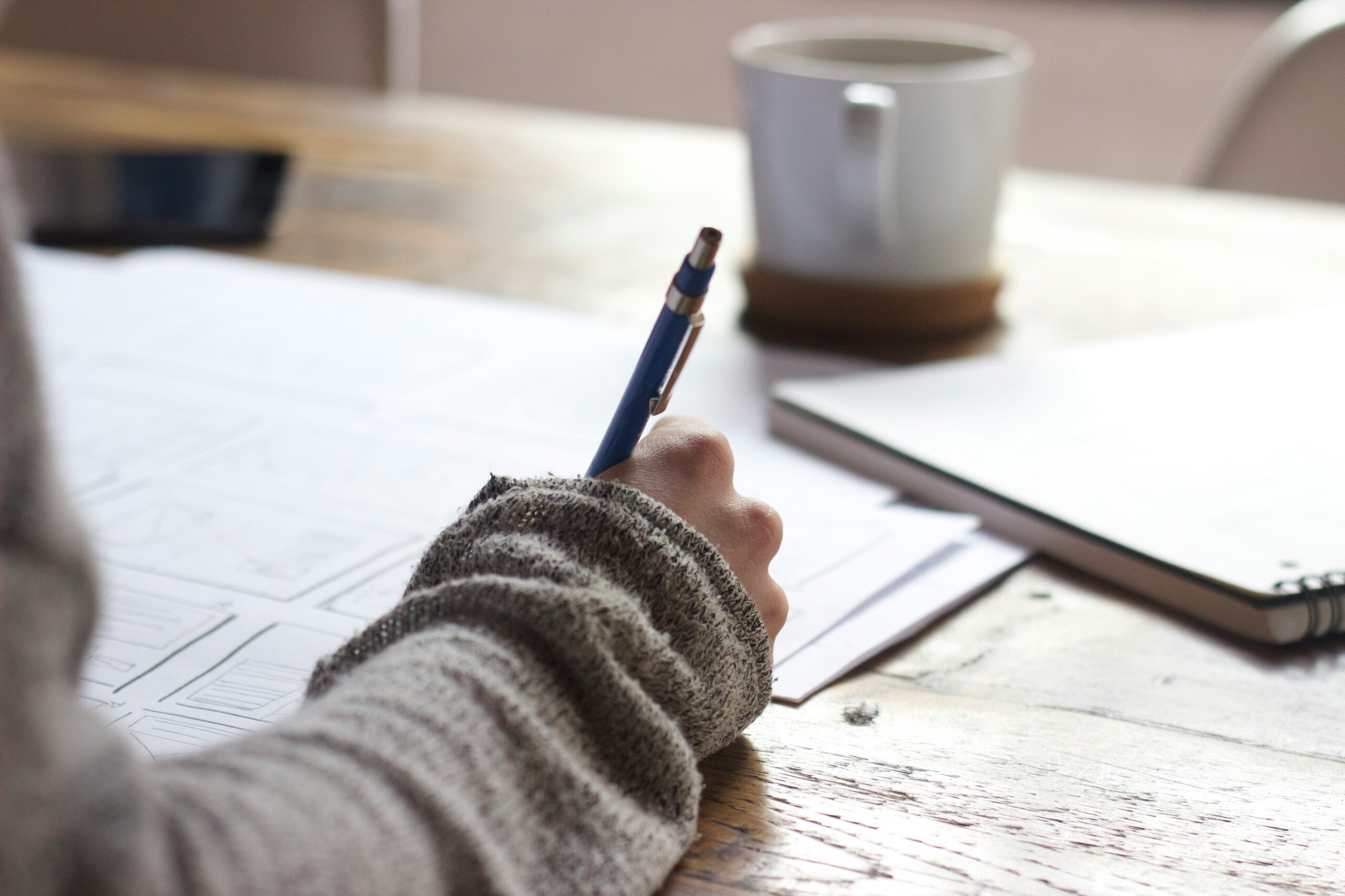 Hand schrijft op plattegrond met potlood en koffie — voorstel interieurontwerp werkwijze